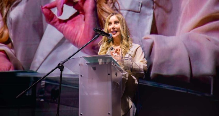 Ministra Diana Morales hablando por micrófono al público, desde atril en el escenario.